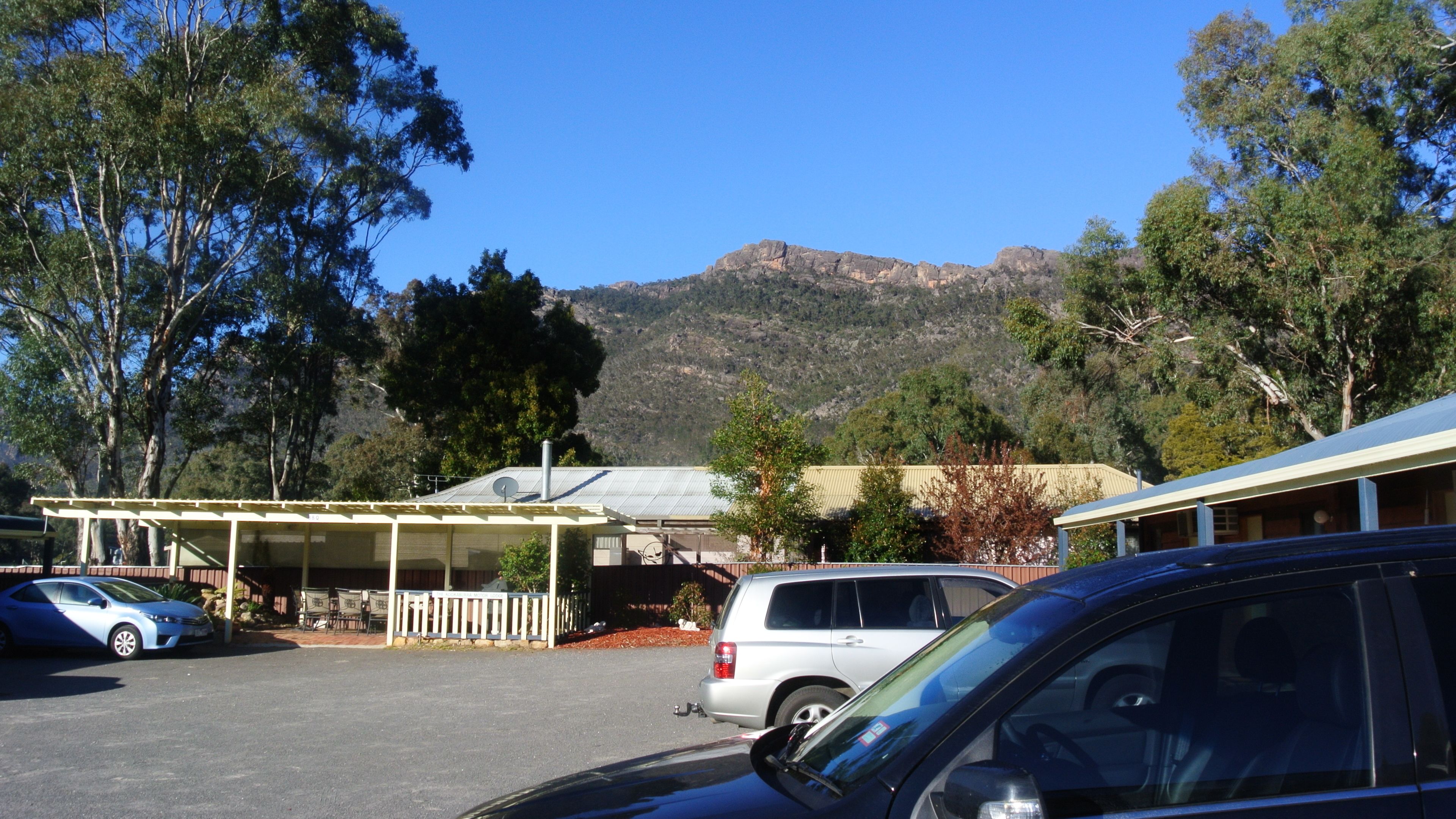 A parking area with cars, a covered structure, and a mountain in the background.