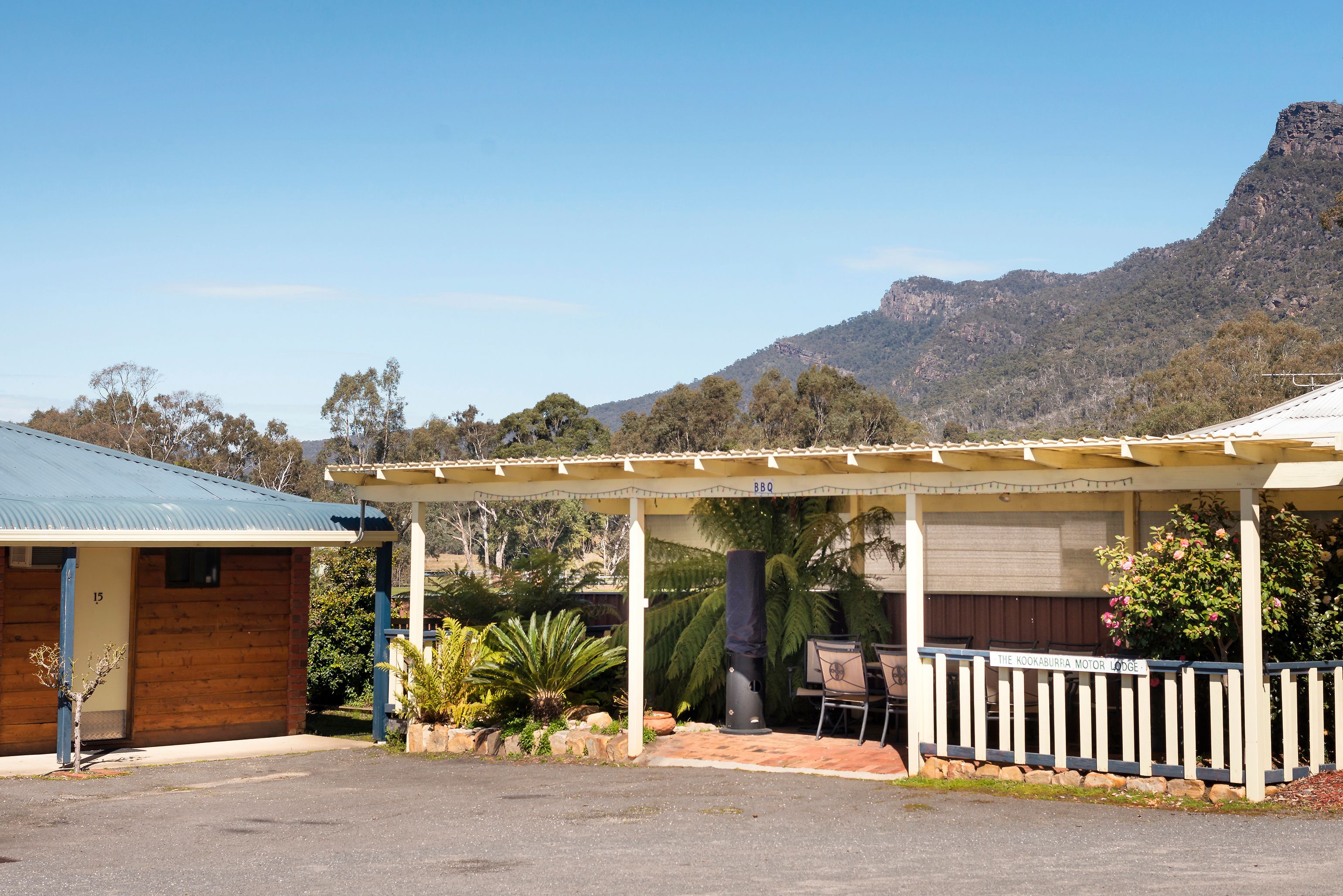 A motor lodge with a covered outdoor seating area, a BBQ, and a view of a mountain.