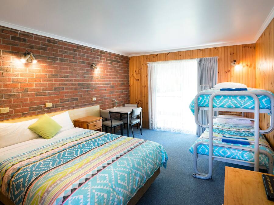 Ett hotellrum med en tegelvägg, träpanel, en våningssäng, ett skrivbord och en tv.