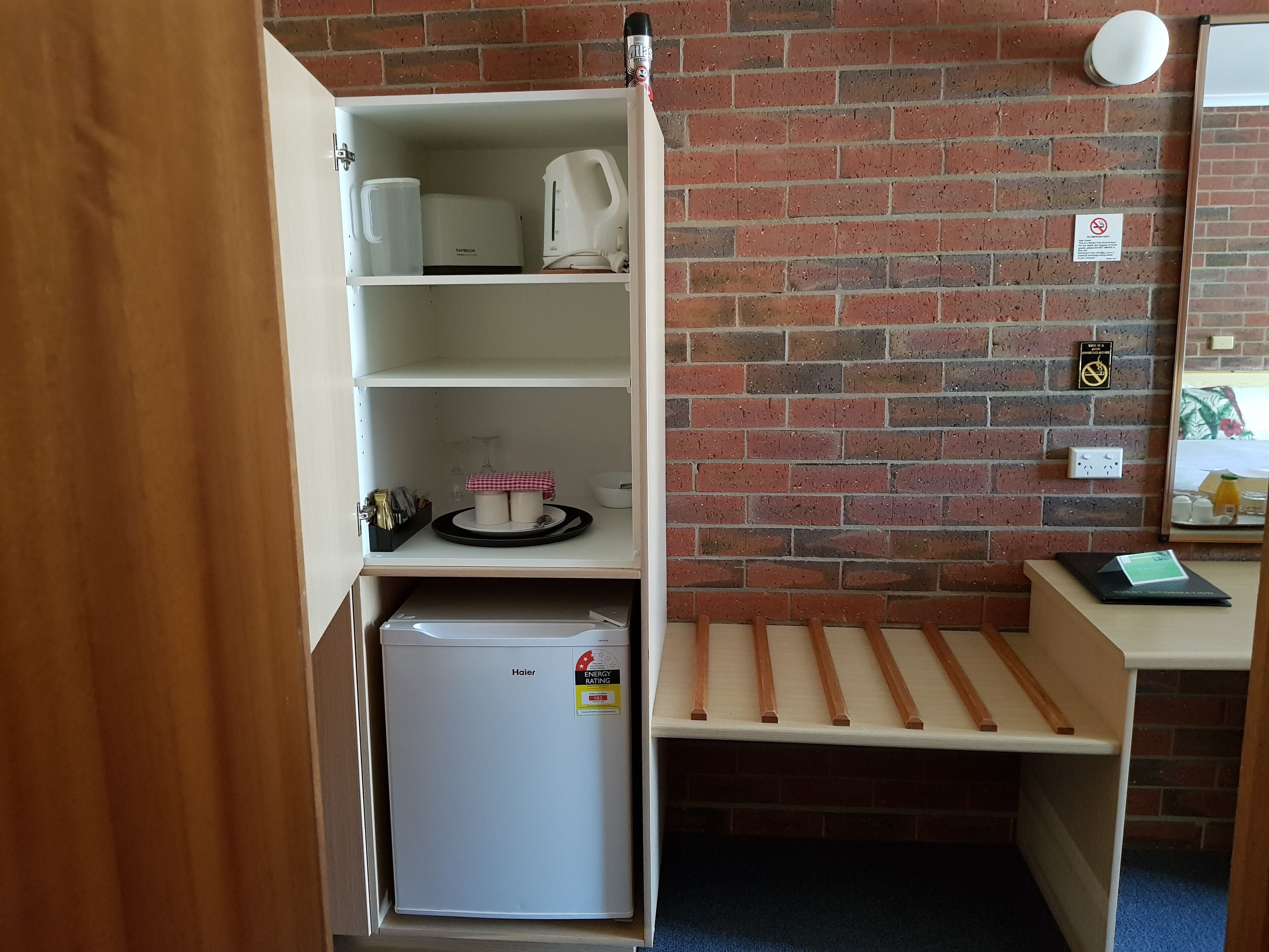 A compact kitchenette with a refrigerator, a kettle, a toaster, and a coffee maker on the shelves.