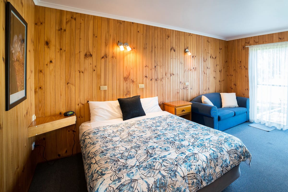 Ein Zimmer mit einem Bett, einem Schlafsofa, einem Tisch und einem fensterbepflanzten Fenster.