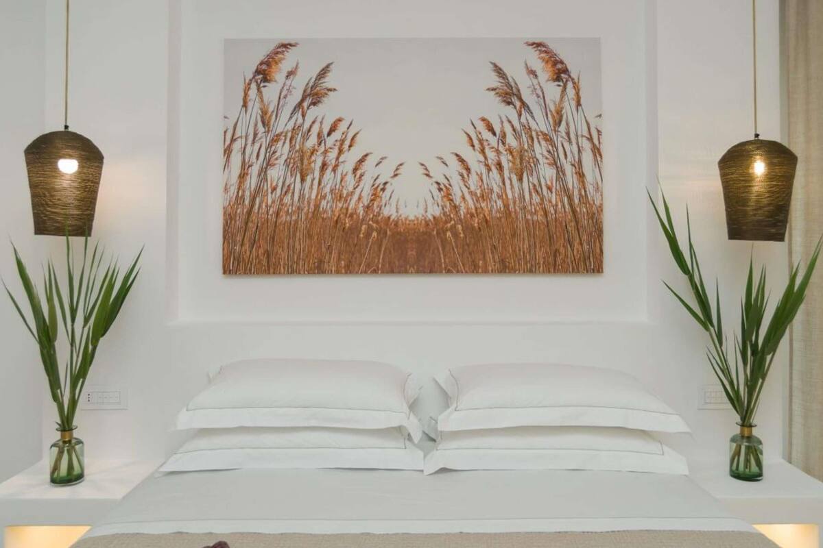 Un dormitorio con una cama, dos mesitas de noche, un cuadro colgado en la pared y dos lámparas colgantes.