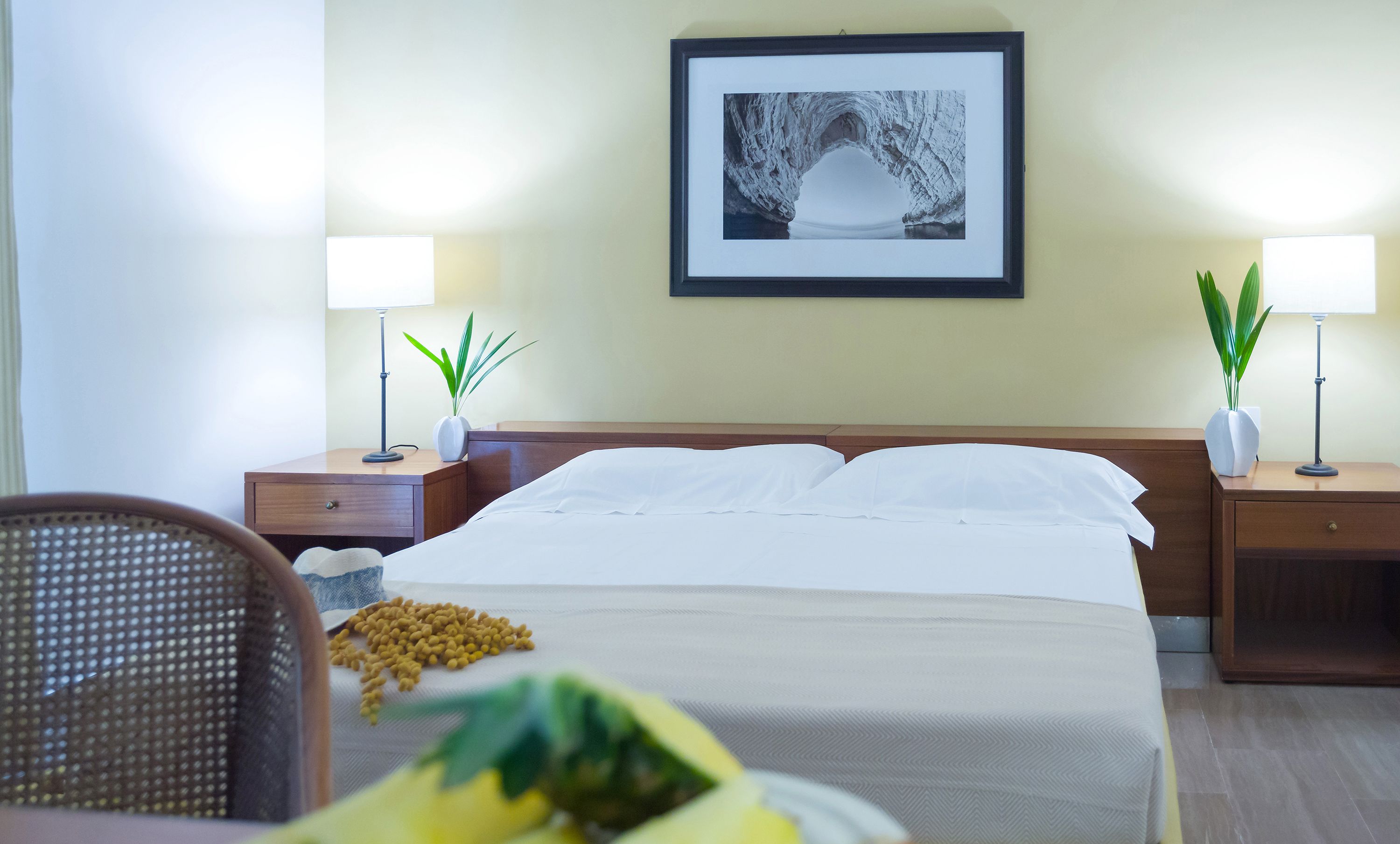 Une chambre d’hôtel avec un lit, deux tables de chevet avec des lampes, un tableau encadré au mur et une chaise.