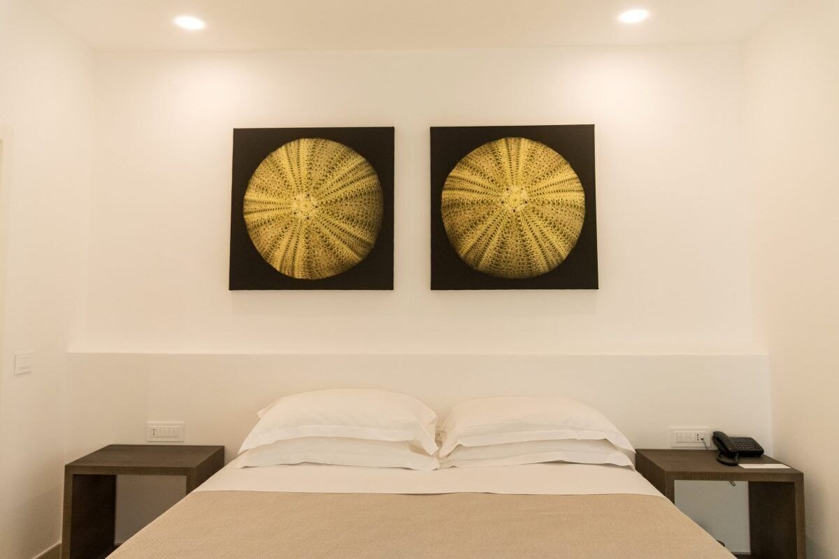 Een hotelkamer met een bed, twee nachtkastjes en twee kunstwerken aan de muur.
