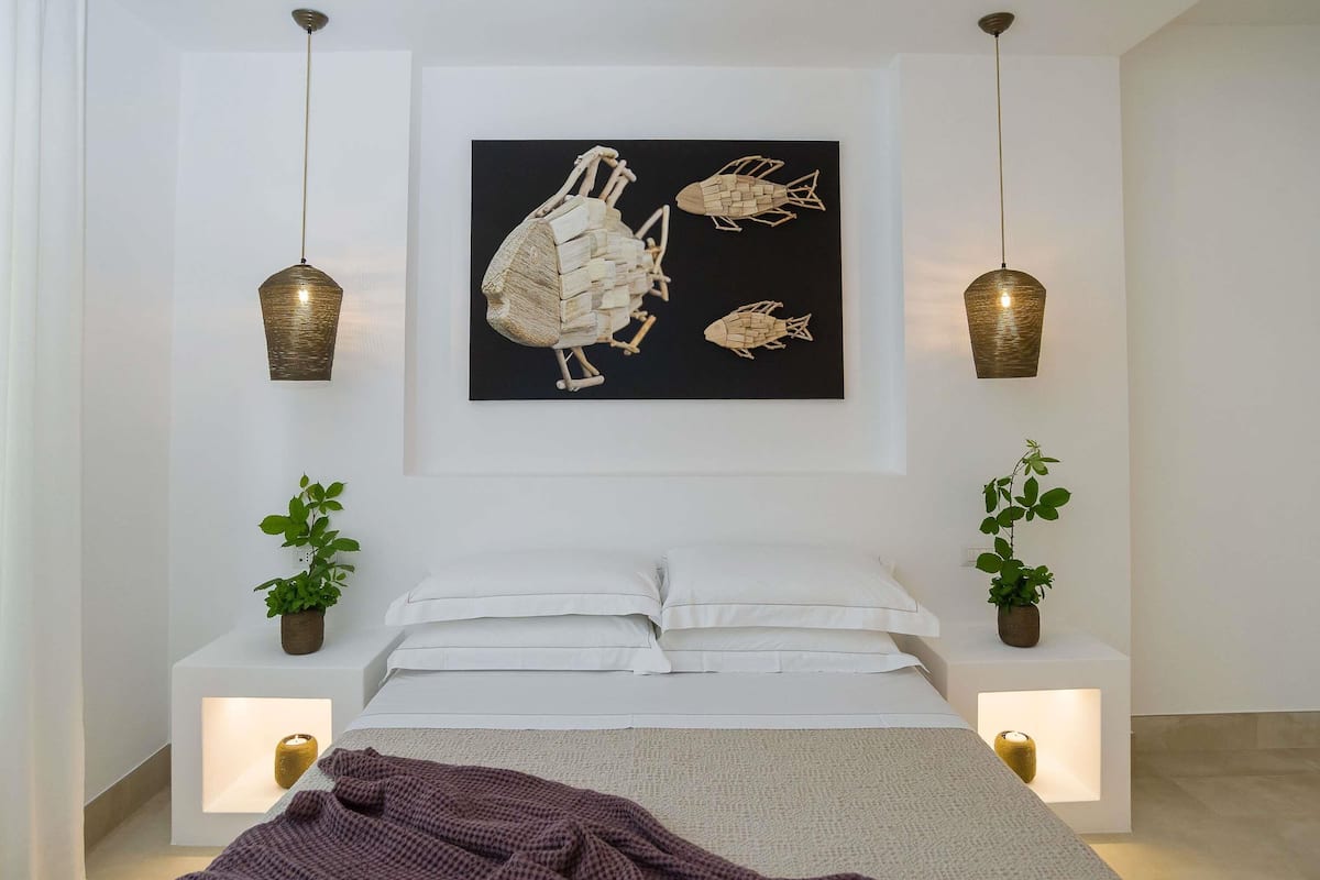 A modern bedroom with a bed, two bedside tables, a wall-mounted artwork, and pendant lights.