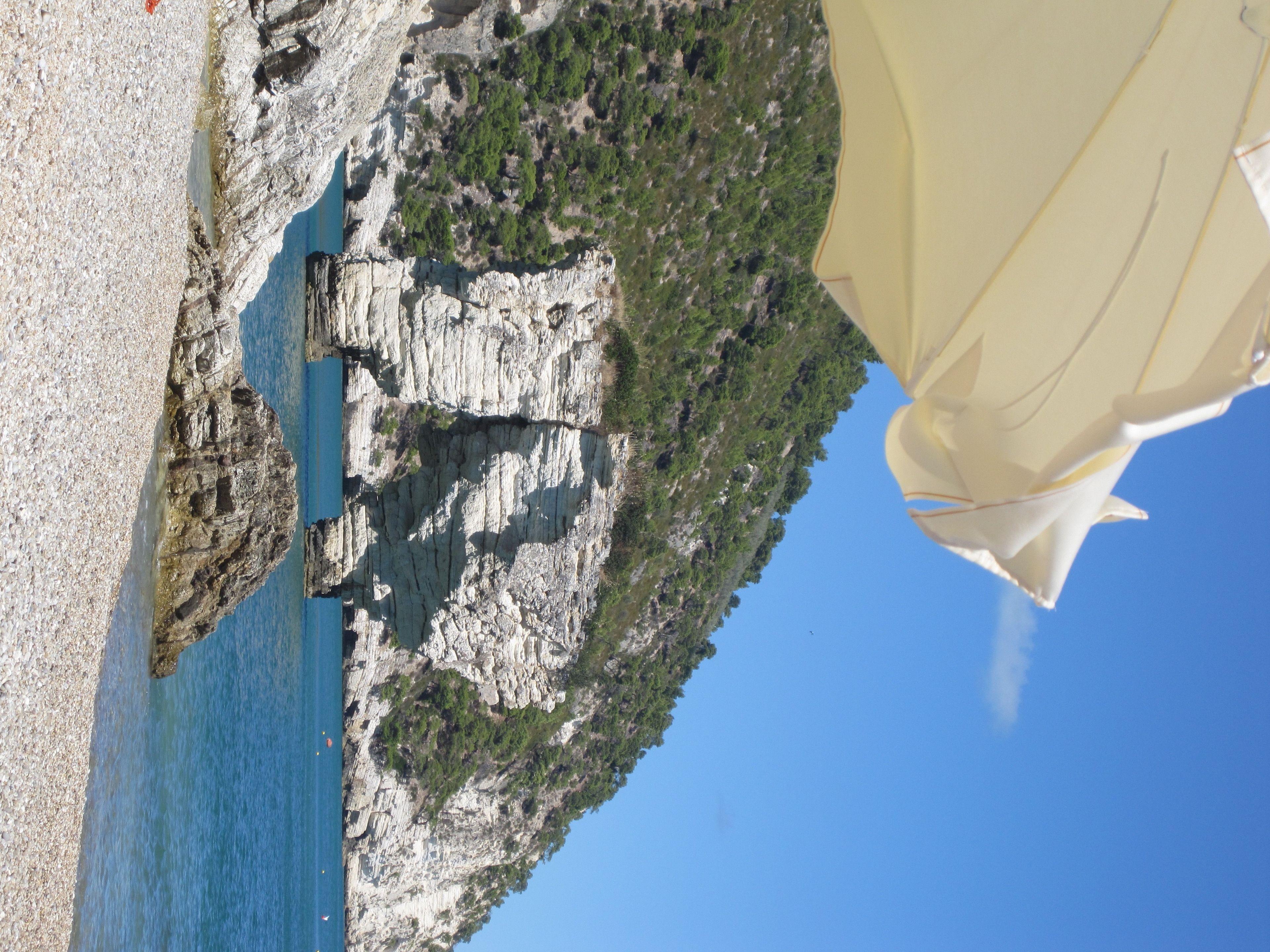 Una scogliera a picco sul mare con una spiaggia rocciosa e un mare cristallino blu.