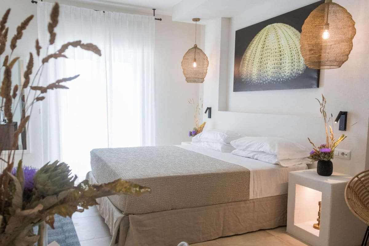 Un dormitorio moderno con una cama grande, dos lámparas de noche, una obra de arte en la pared y una mesita con un florero.