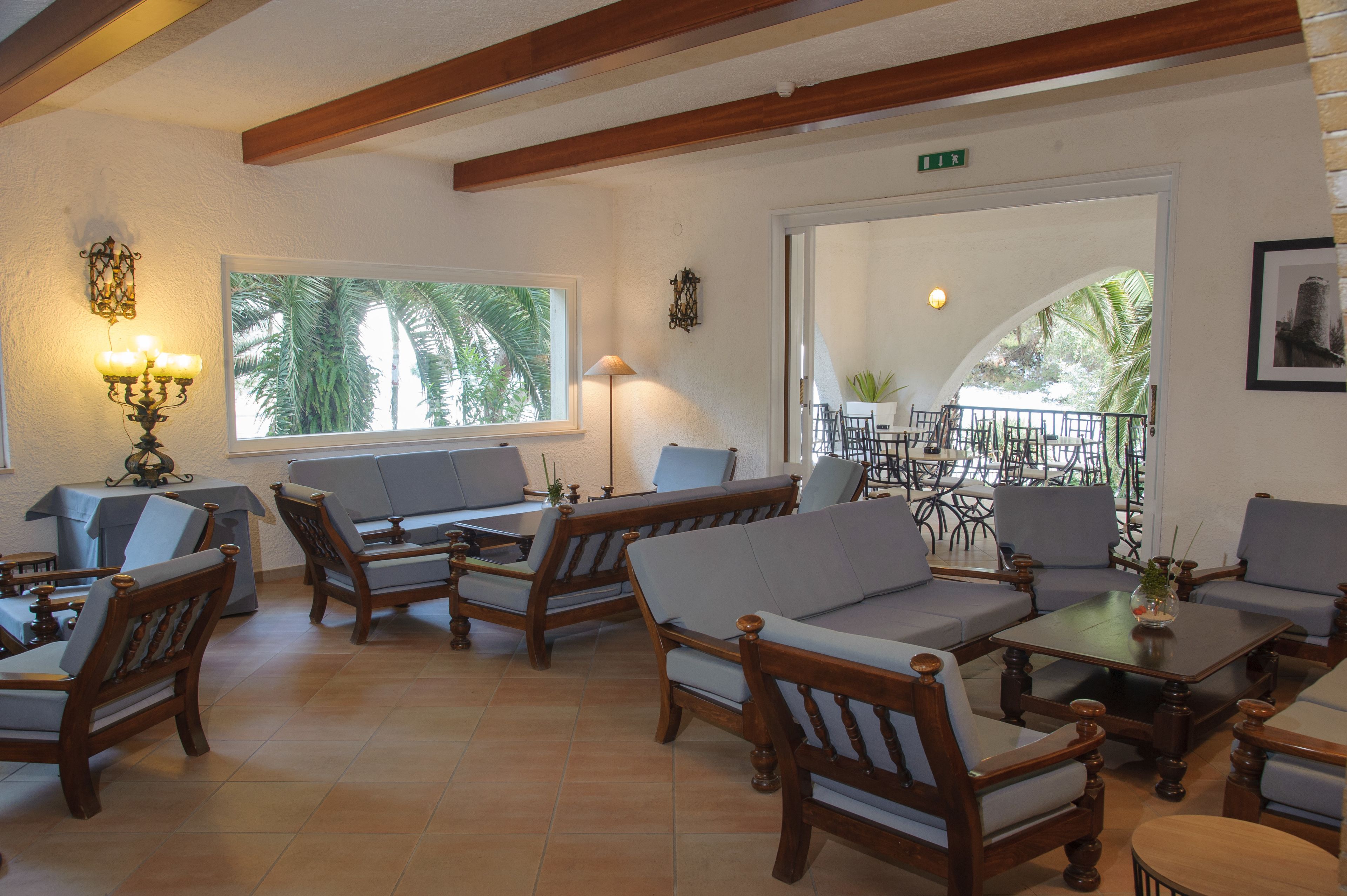 A cozy lounge area with wooden furniture and a large window offering a view of palm trees.