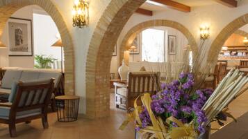 Une pièce avec des arches en briques, des meubles en bois et un vase rempli de fleurs violettes.