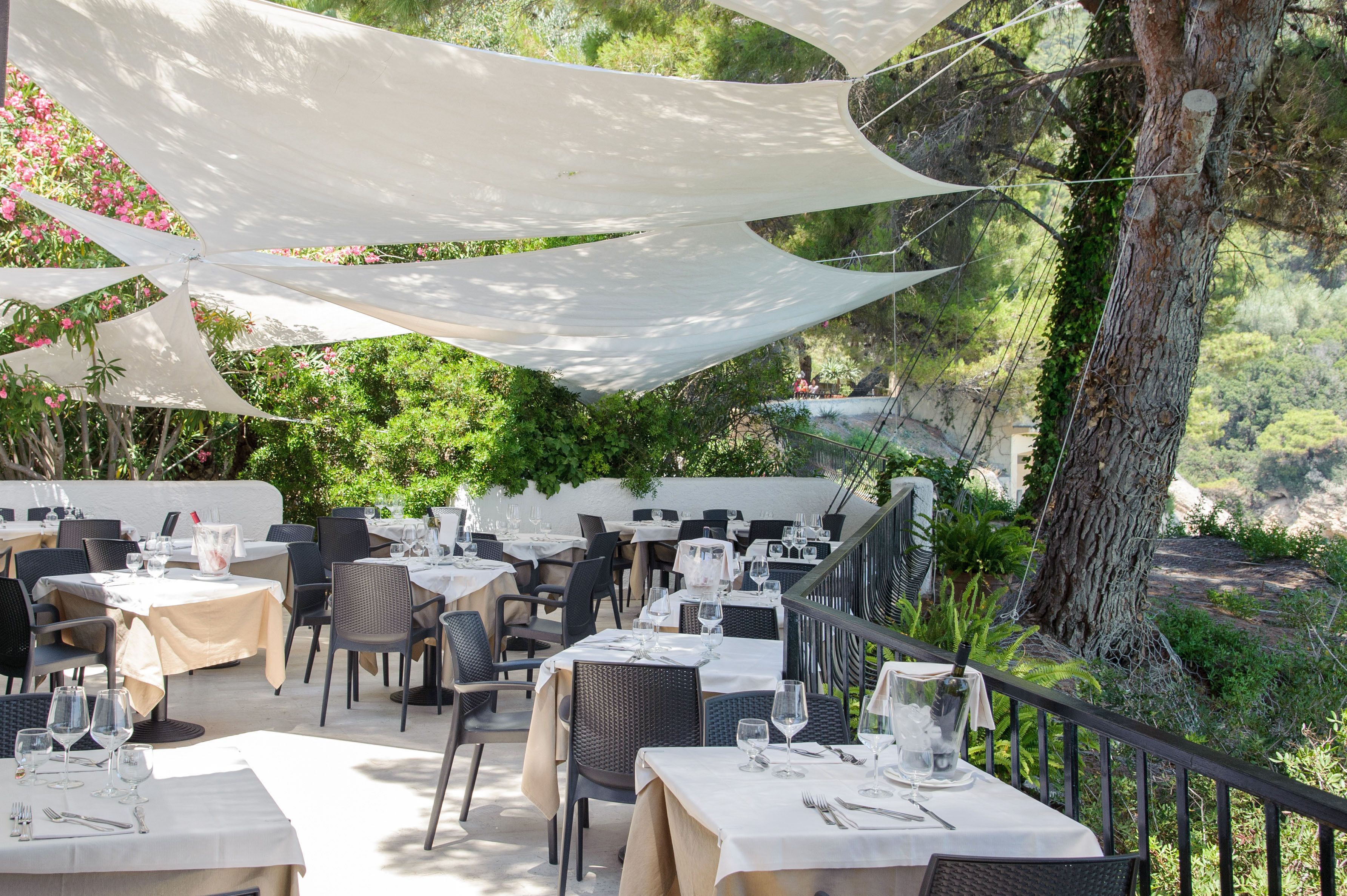An outdoor dining area with tables set for guests, surrounded by greenery and overlooking a scenic landscape.