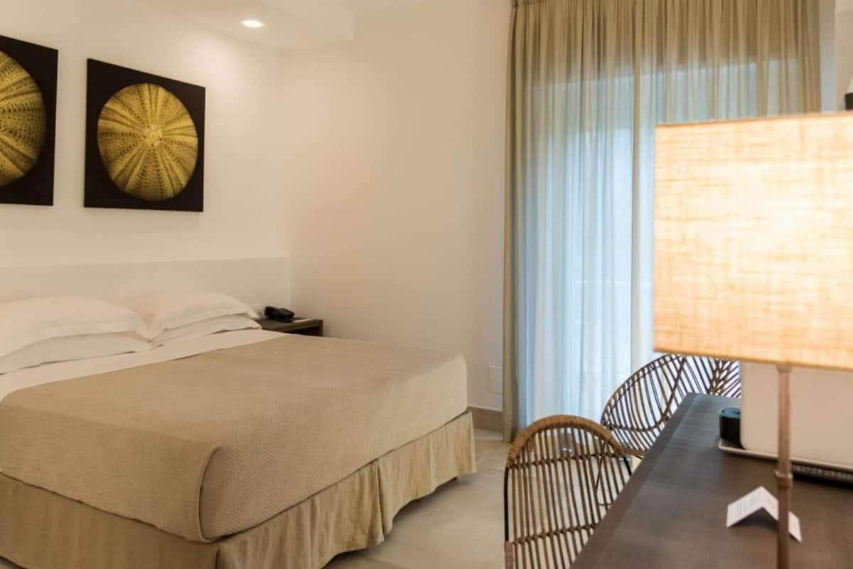 Una habitación de hotel con cama, un escritorio con lámpara y dos elementos decorativos colgados en la pared.