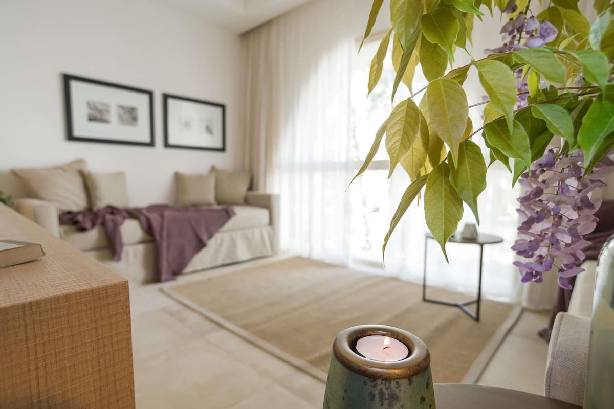 Una sala de estar con un sofá, una mesita de centro con una vela y una planta colgante.