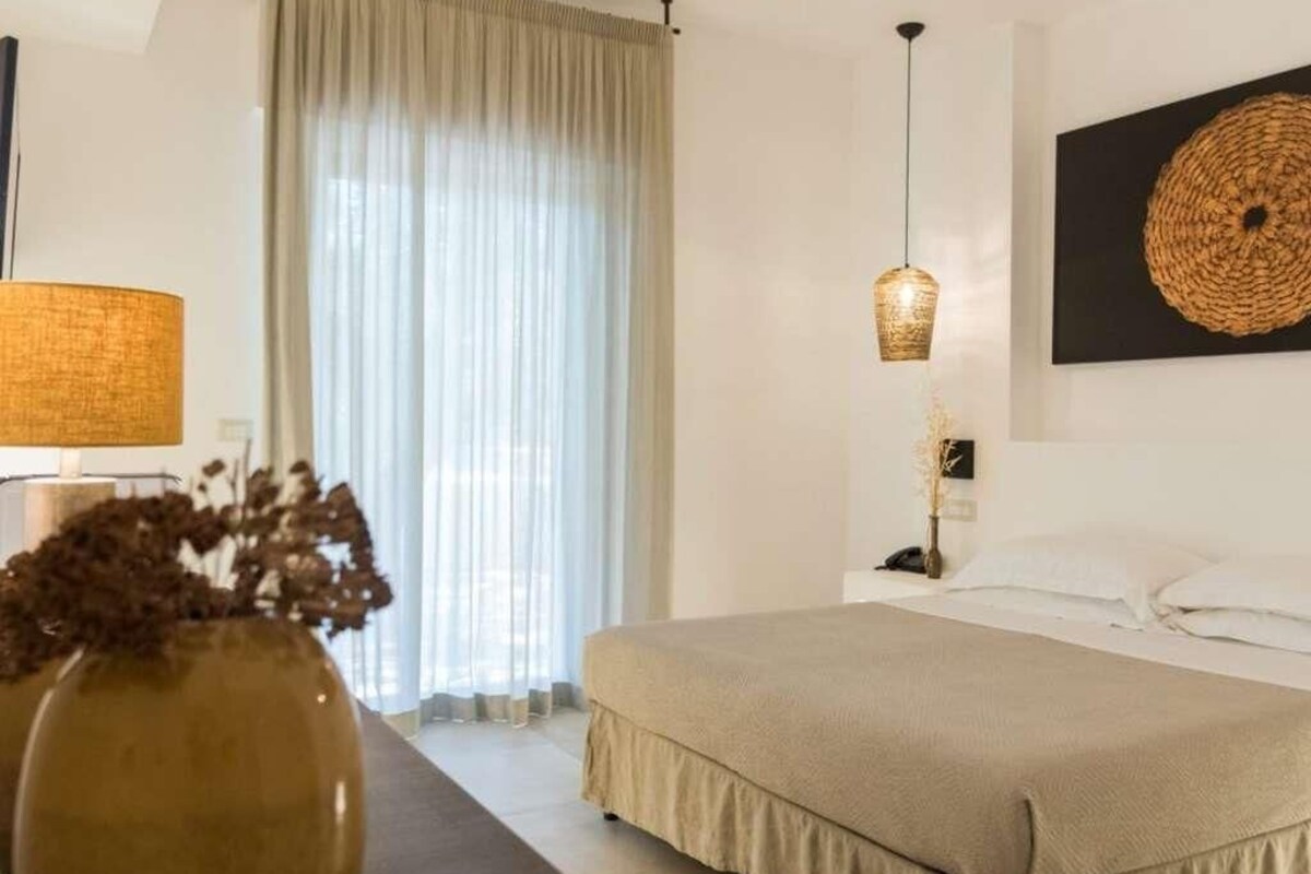 Een slaapkamer met een bed, nachtkastje, lamp en een kunstwerk aan de muur.
