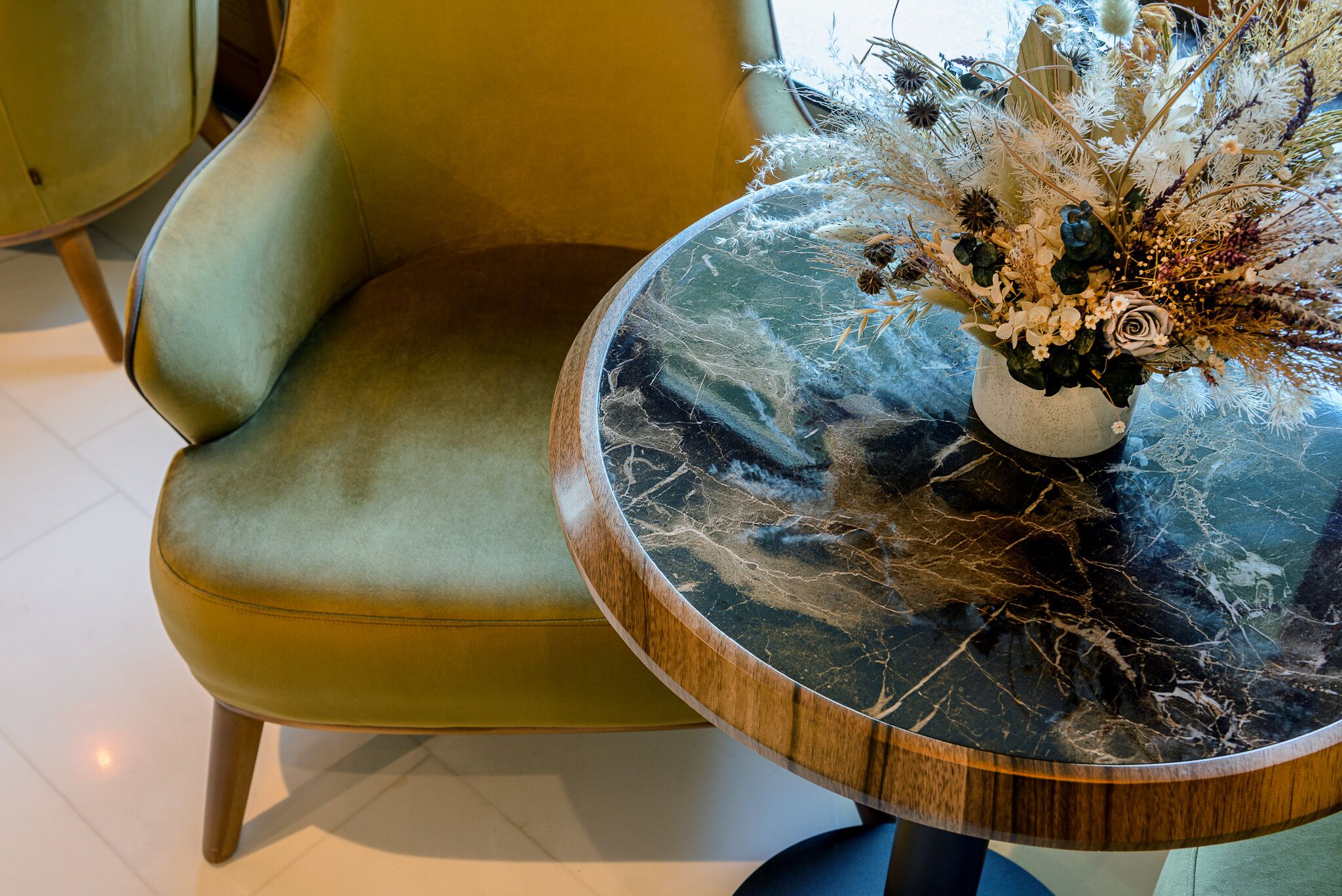 A round table with a marble top and a vase of dried flowers.