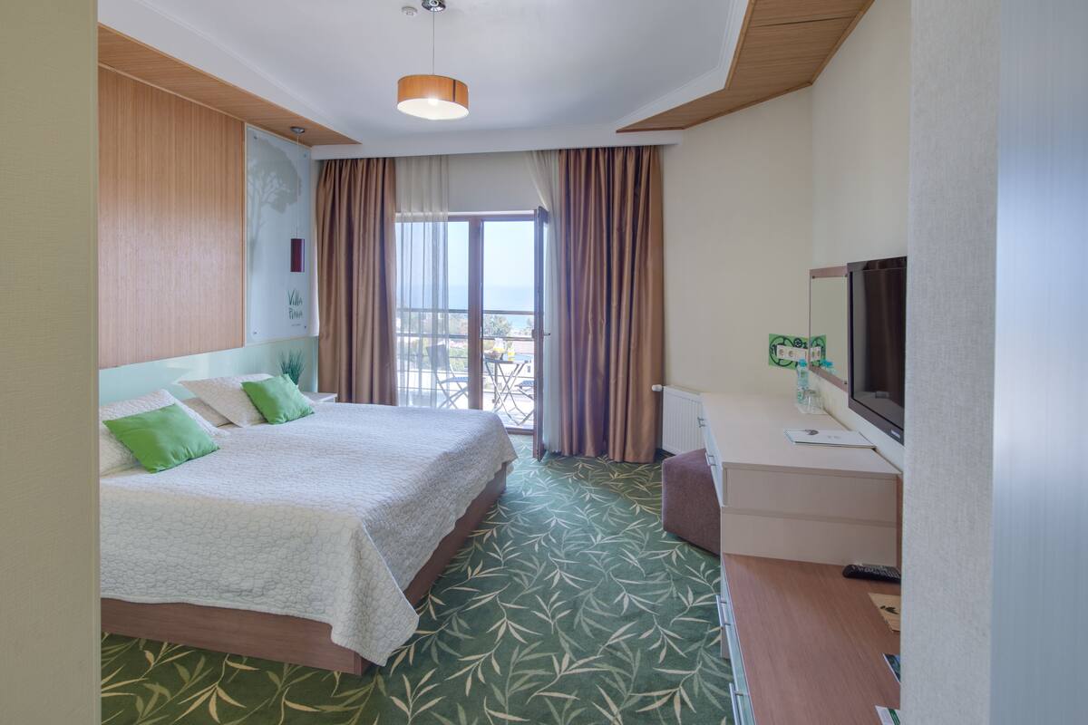 A hotel room with a bed, a desk, a television, and a window with curtains.
