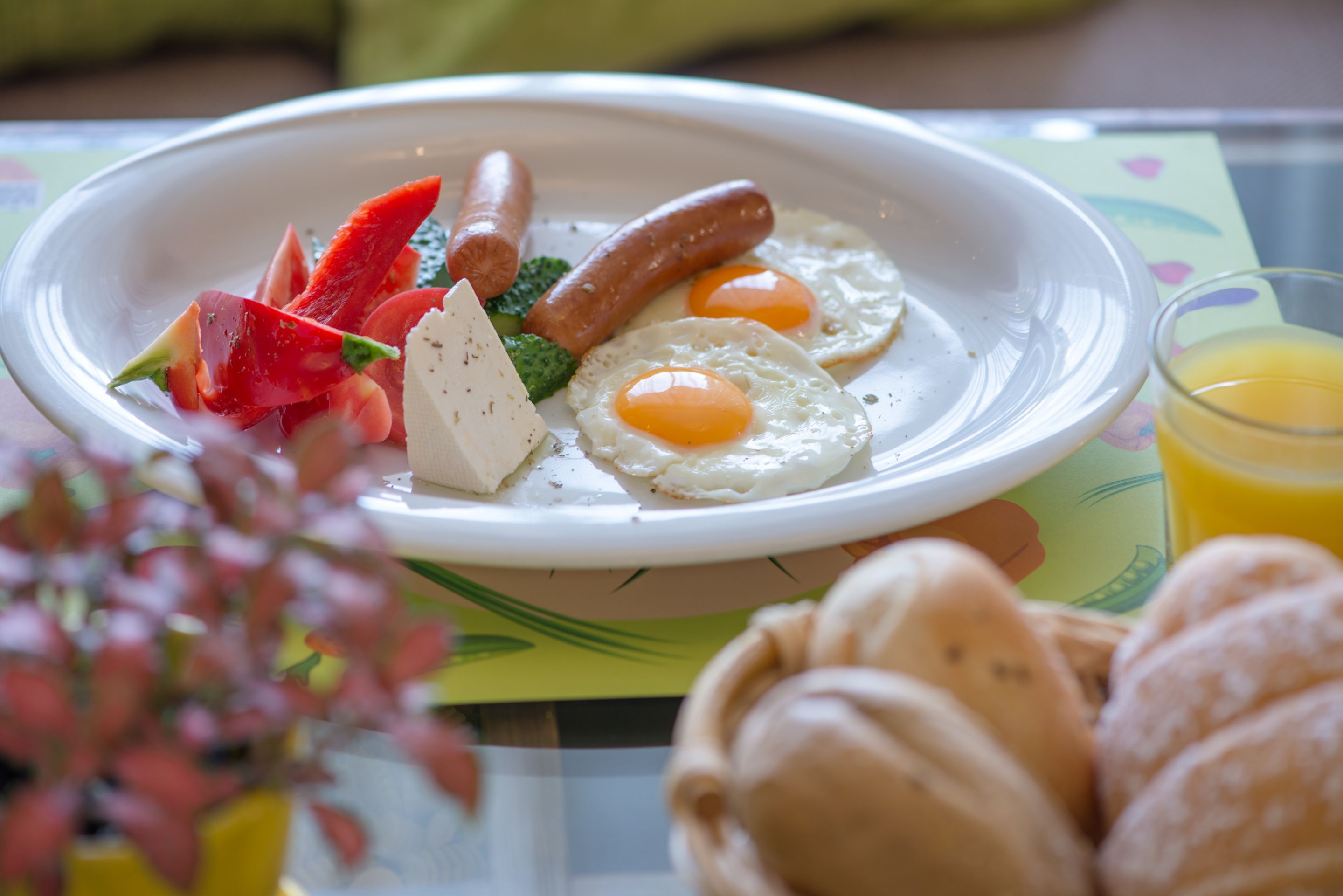 A breakfast plate with eggs, sausages, and strawberries, accompanied by croissants and a glass of orange juice.