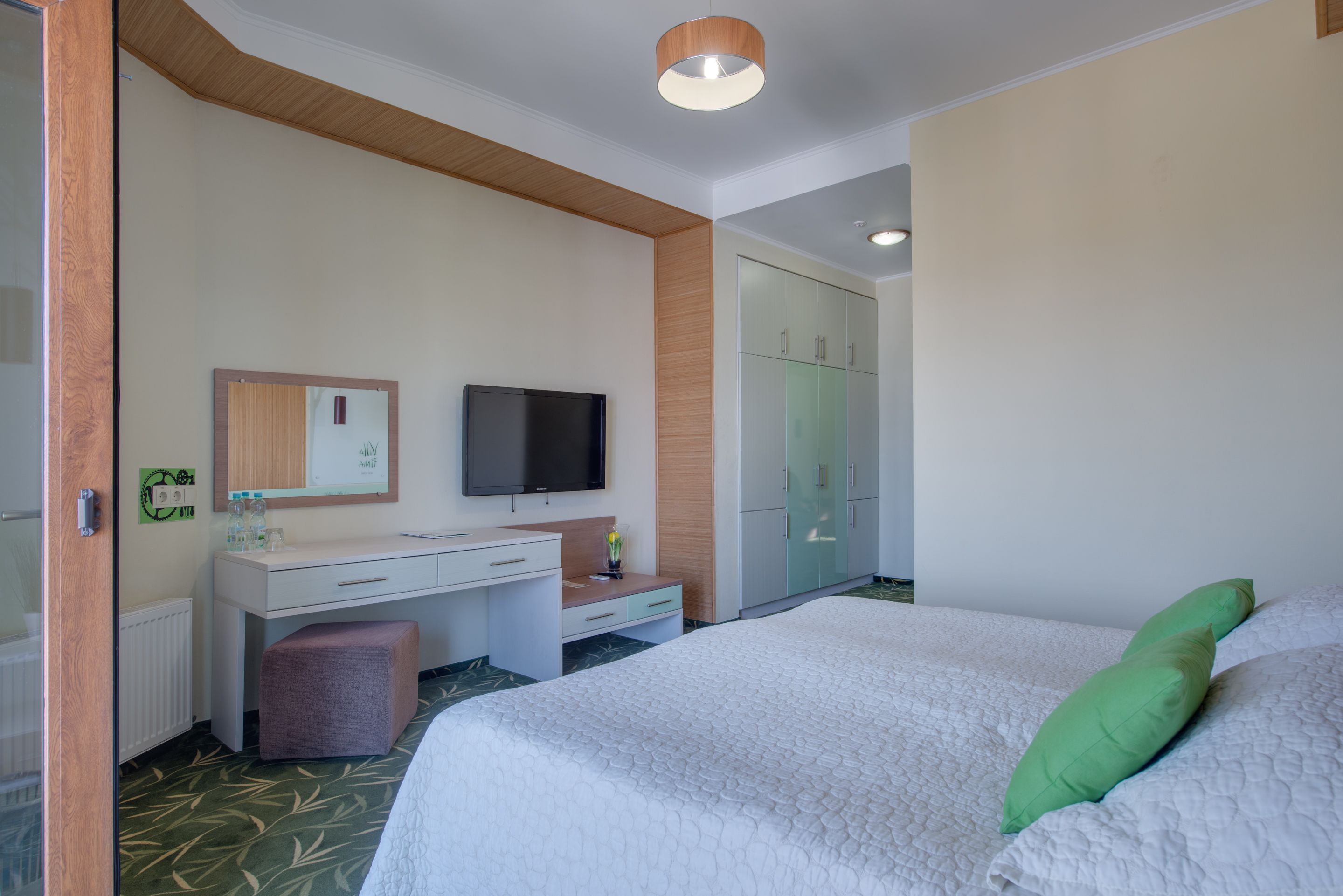 A hotel room with a bed, a desk, a television, a wardrobe, and a mirror.