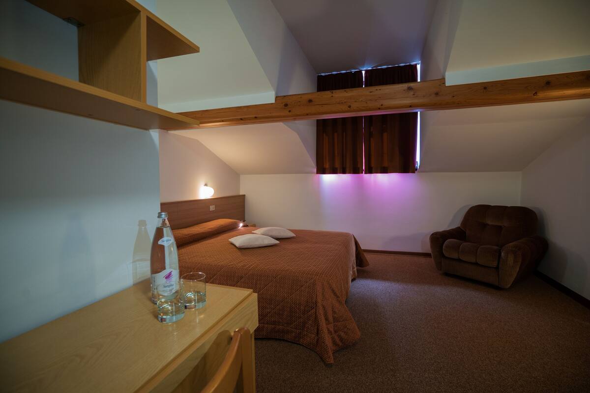 A bedroom with a bed, a chair, a desk, and a window with curtains.