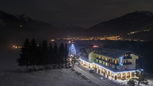 Un hotel con un paisaje nevado, un árbol de Navidad iluminado y montañas al fondo.