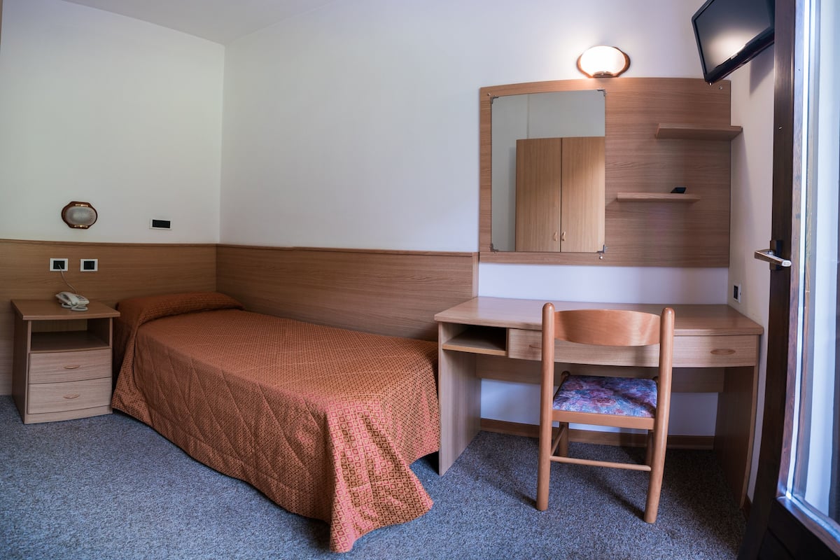 A bedroom with a bed, a desk, a chair, a TV, and a mirror.
