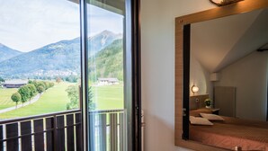 A bedroom with a large window offering a view of a mountainous landscape and a distant building.