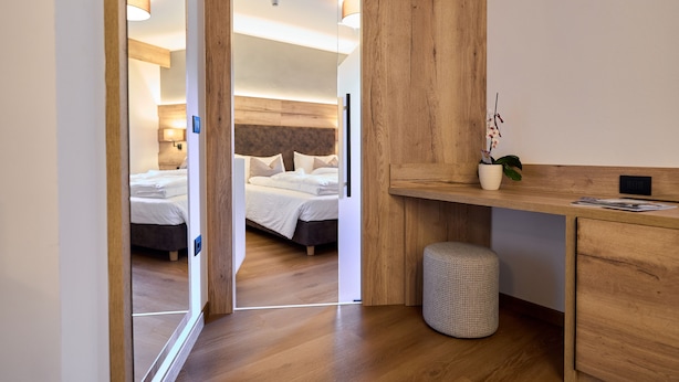 Una habitación de hotel moderna con piso de madera, una cama con sábanas blancas, un escritorio con una planta y un cesto de basura pequeño.