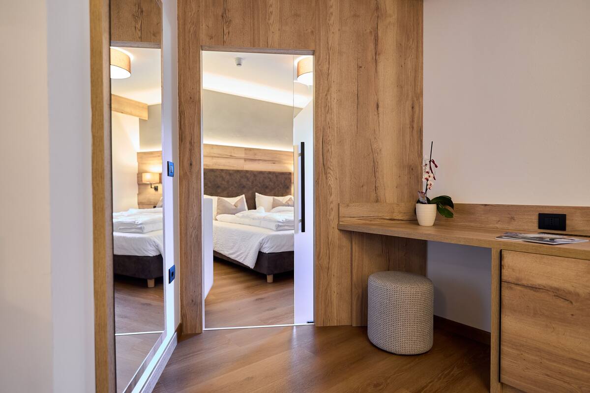 A modern hotel room with a wooden floor, a bed with white linens, a desk with a plant, and a small waste bin.