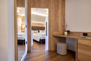 A modern hotel room with a wooden floor, a bed with white linens, a desk with a plant, and a small waste bin. - Hotel Rio (Caderzone Terme)