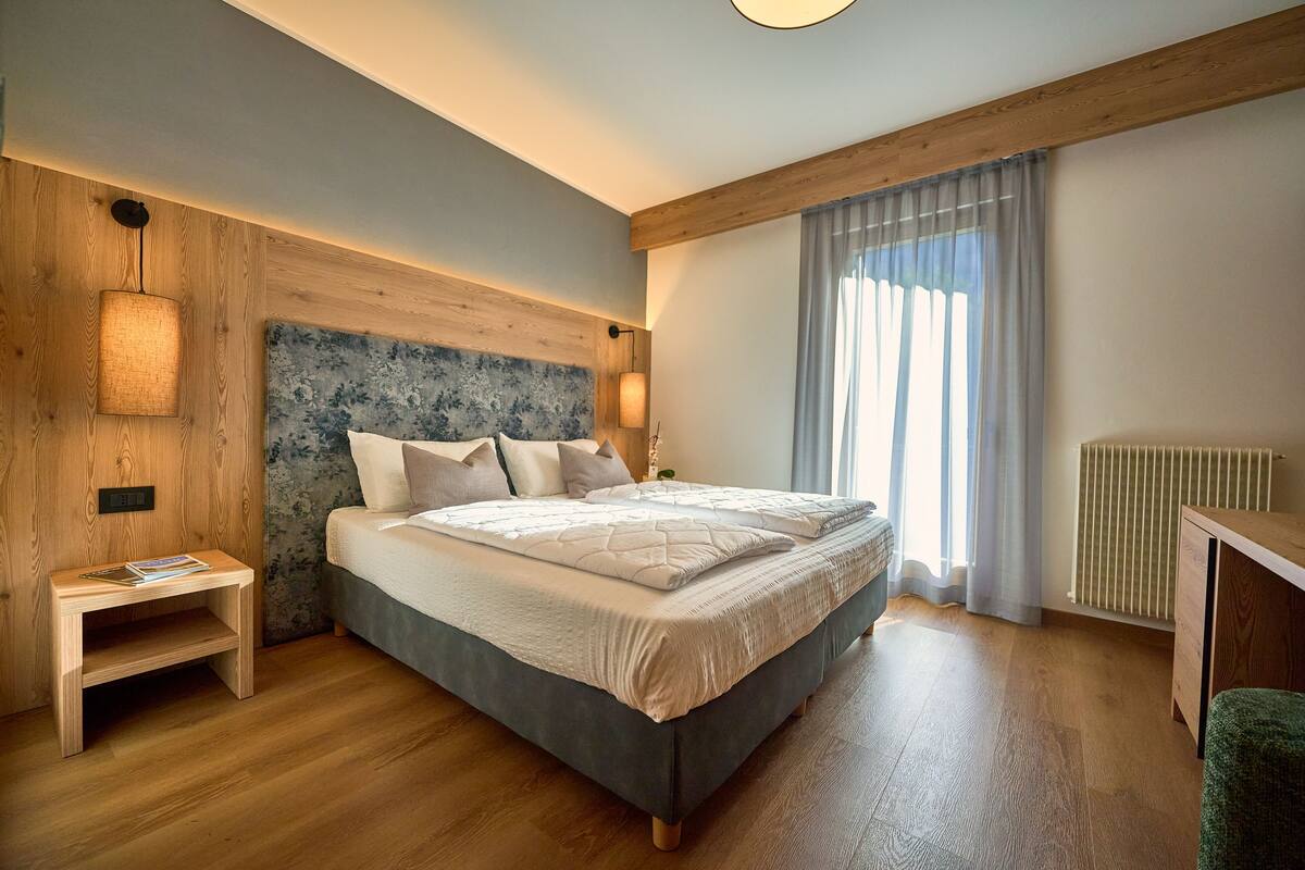 A bedroom with a wooden headboard, a bedside table with a lamp, a bed with a quilt, and a radiator.
