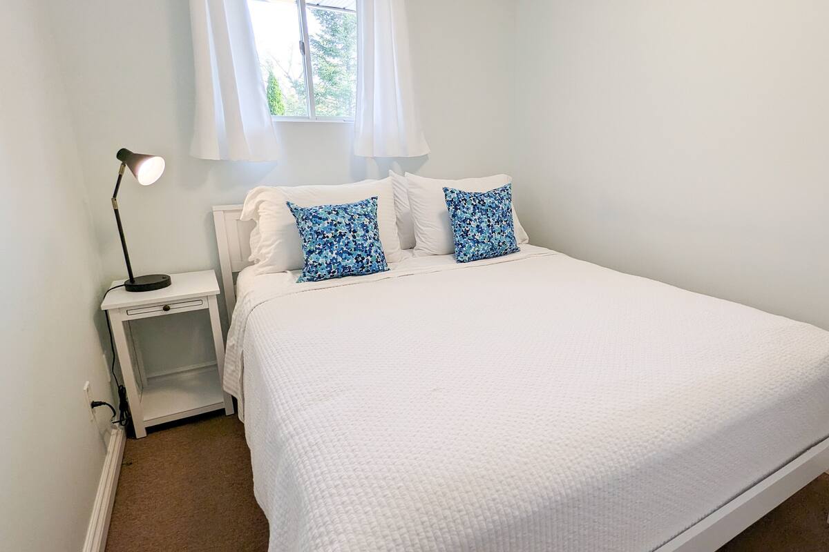 A white bed with two blue floral pillows, a white nightstand, and a floor lamp.