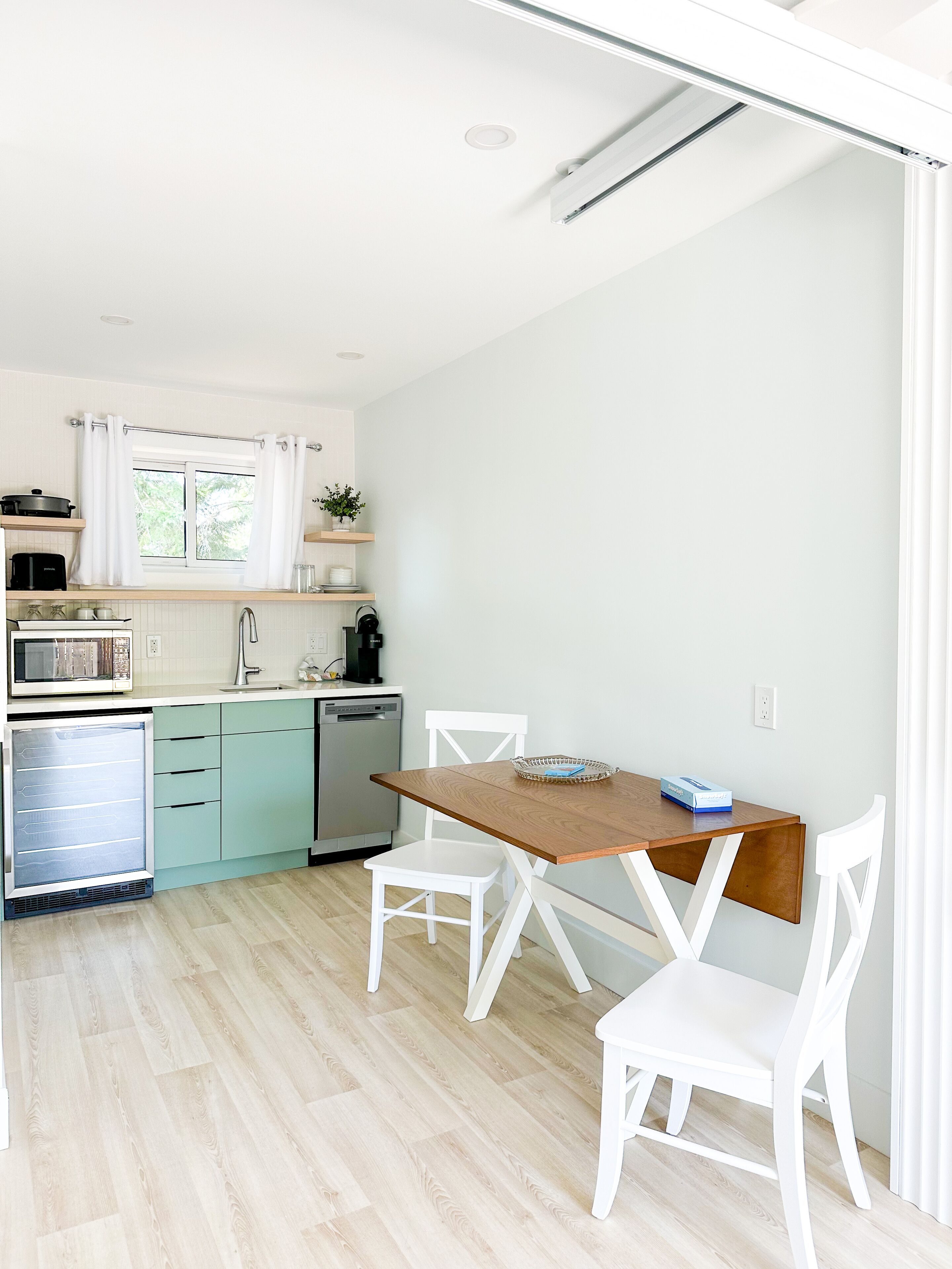 A compact kitchen with a dining area, including a wooden table and white chairs, a built-in oven, and a microwave.