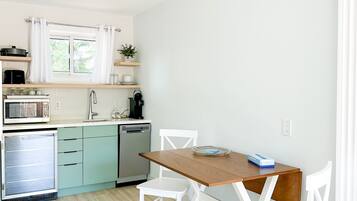 A compact kitchen with a dining area, including a wooden table and white chairs, a built-in oven, and a microwave.