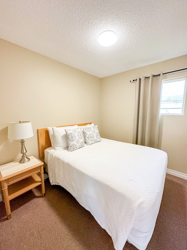 Une chambre à coucher avec un lit, une table de chevet, une lampe et une fenêtre avec des rideaux.