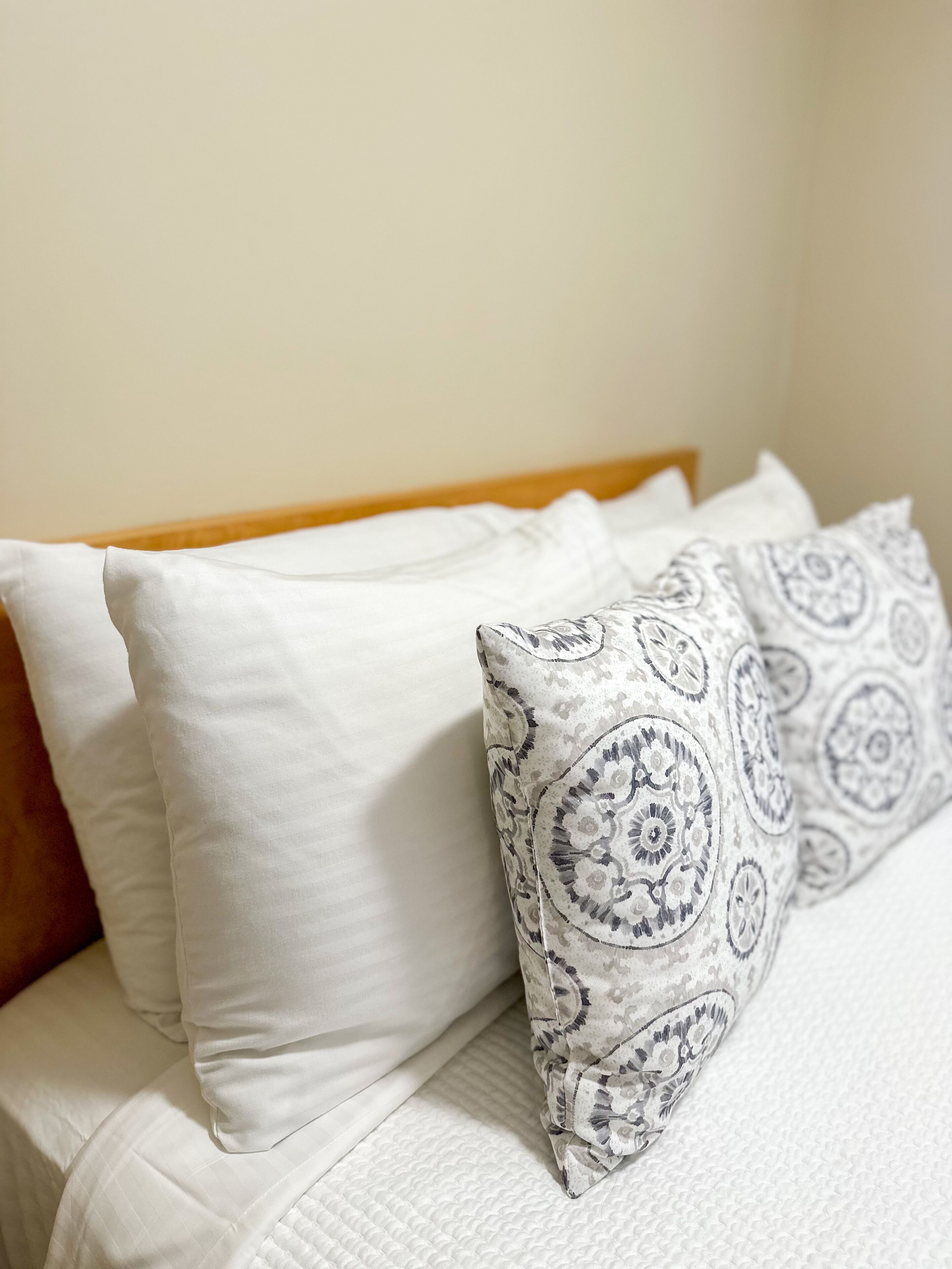 Una cama con almohadas blancas y un cojín estampado.