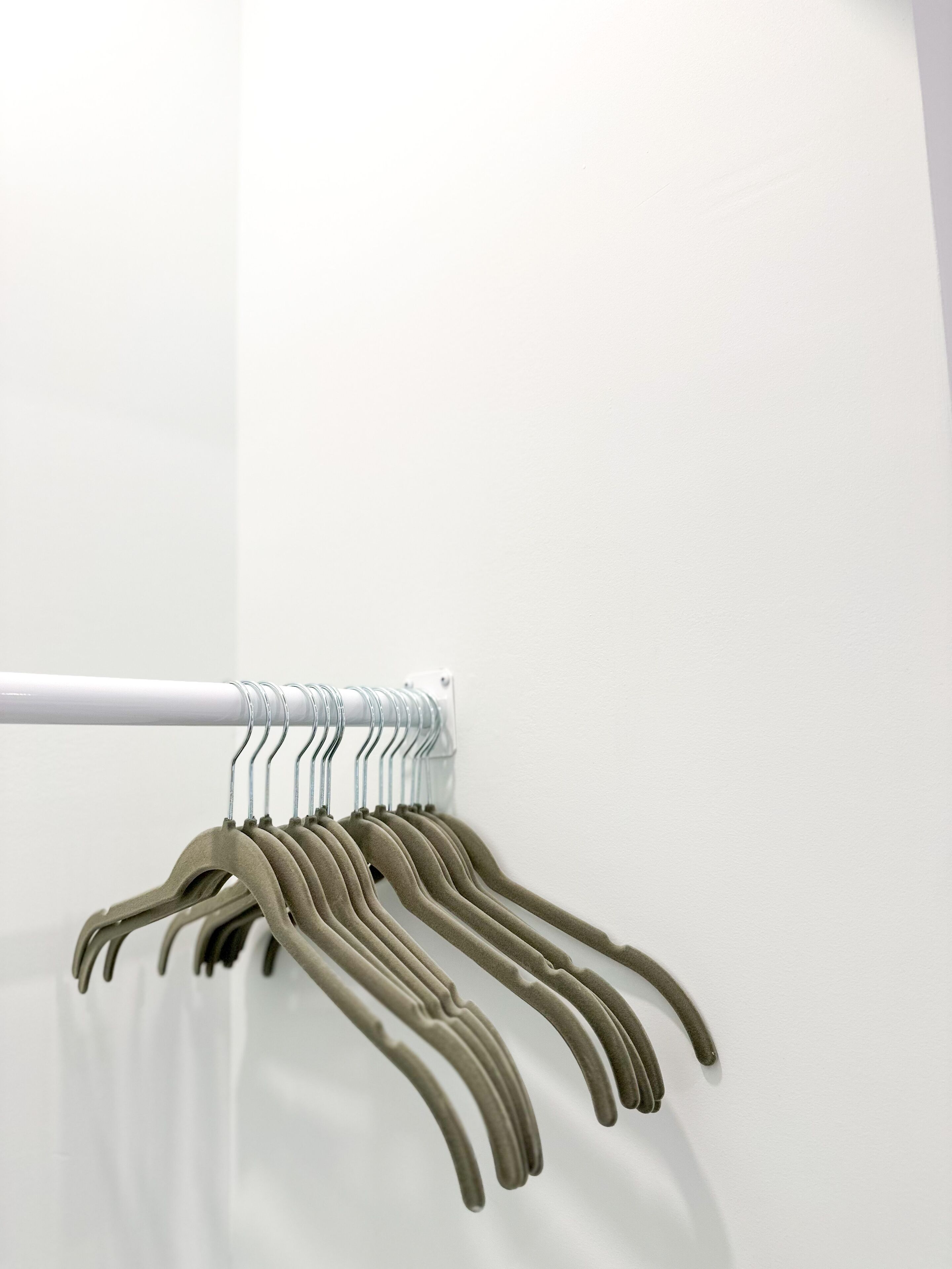 Eine weiße Wand mit einer Metallvorhangstange und mehreren beigen Kleiderbügeln.