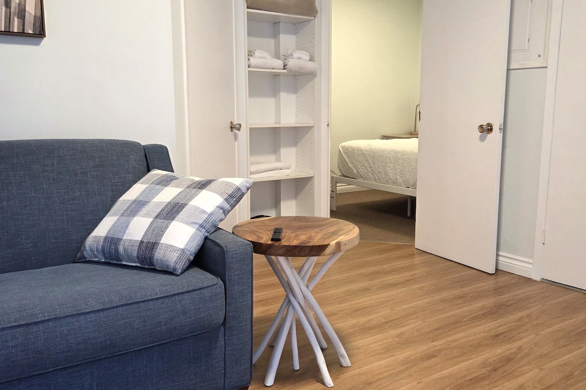 A room with a blue sofa, a small wooden table, a white wardrobe, and a bed with a white duvet.