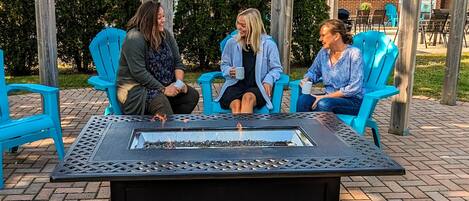 Tres personas sentadas a una mesa con una chimenea al aire libre, bajo una pérgola.