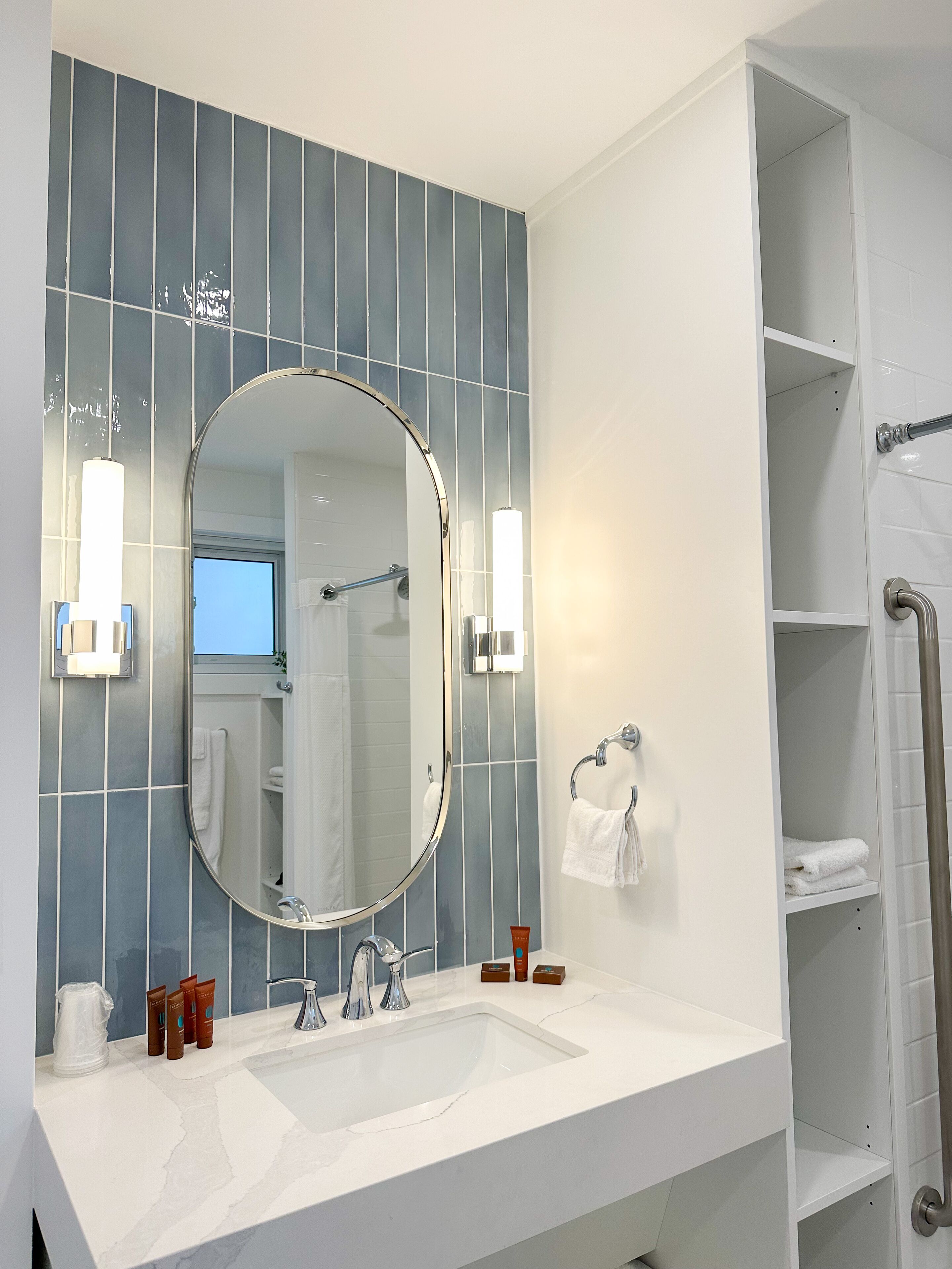 Un baño con un espejo grande, lavamanos blanco y paredes con azulejos azules.