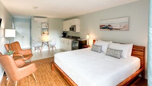 Een hotelkamer met een groot bed, houten vloeren, een kitchenette, een eethoek en een zithoek met stoelen.