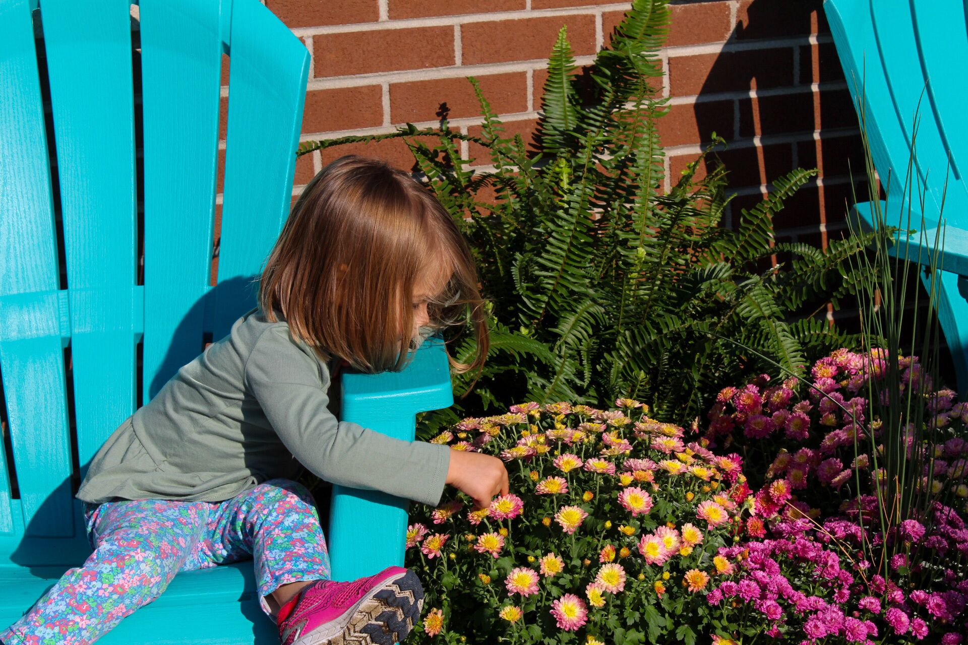 A child sitting on a blue bench next to a garden with various flowers.