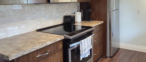 A modern kitchen with dark wood cabinets, a stainless steel refrigerator, a microwave, and a built-in oven.