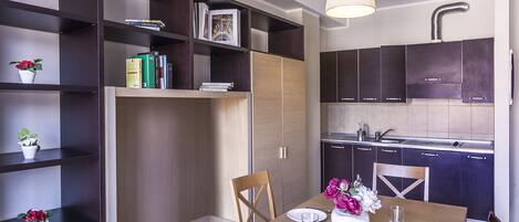 A modern kitchen with dark cabinets, a wooden dining table, and a built-in bookshelf.