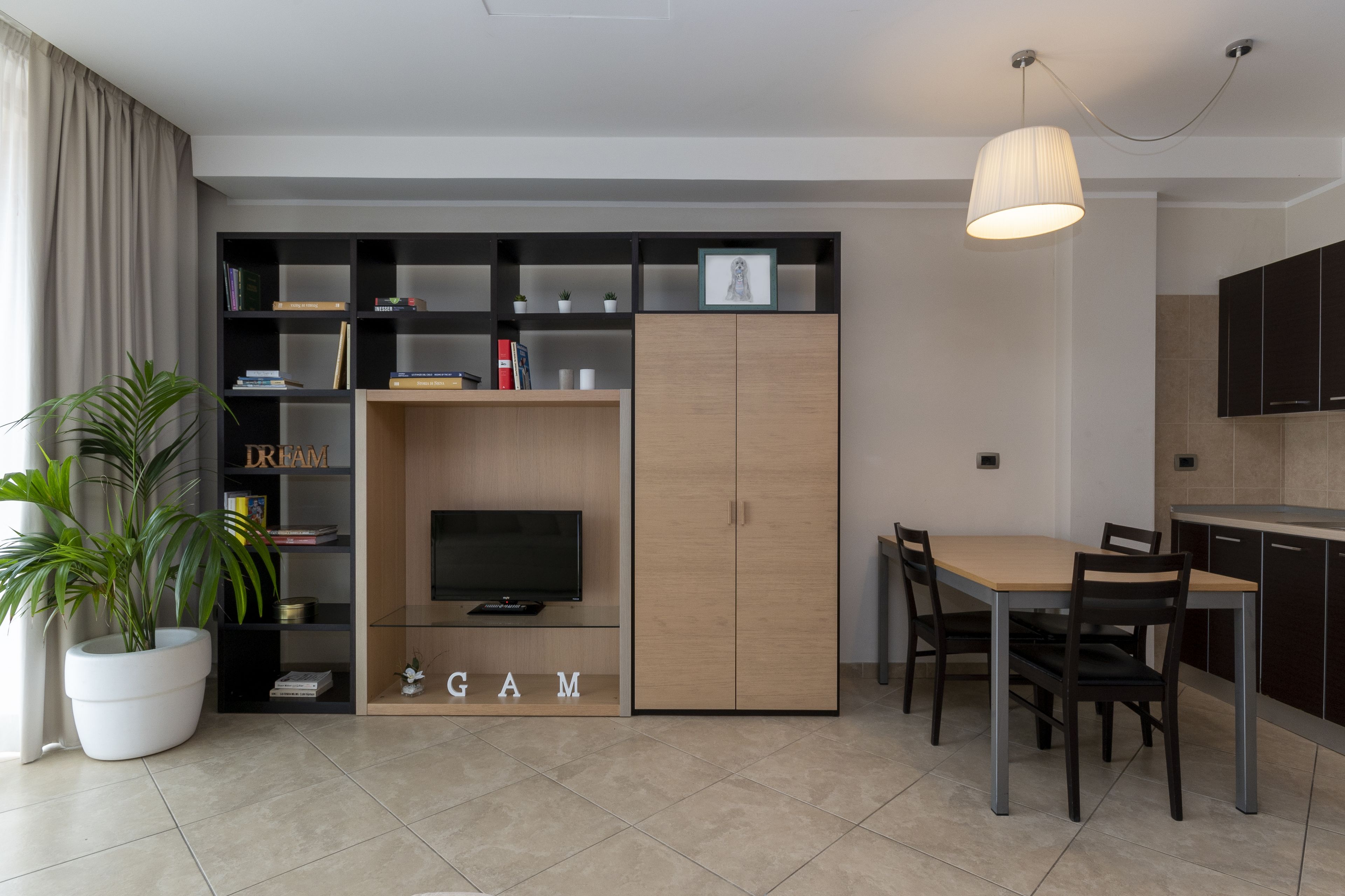 Una sala de estar moderna con televisor, estantería y comedor con mesa y sillas.