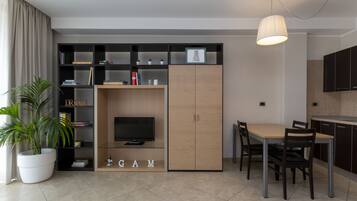 Una sala de estar moderna con televisor, estantería y comedor con mesa y sillas.