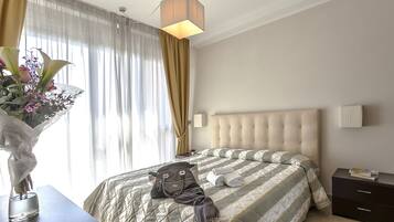 Een opgemaakt bed met een gestreept dekbedovertrek, een nachtkastje met een lamp en een vaas met bloemen op een nachtkastje.