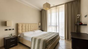 A modern bedroom with a large bed, a bedside table, a desk, and a hanging light fixture.