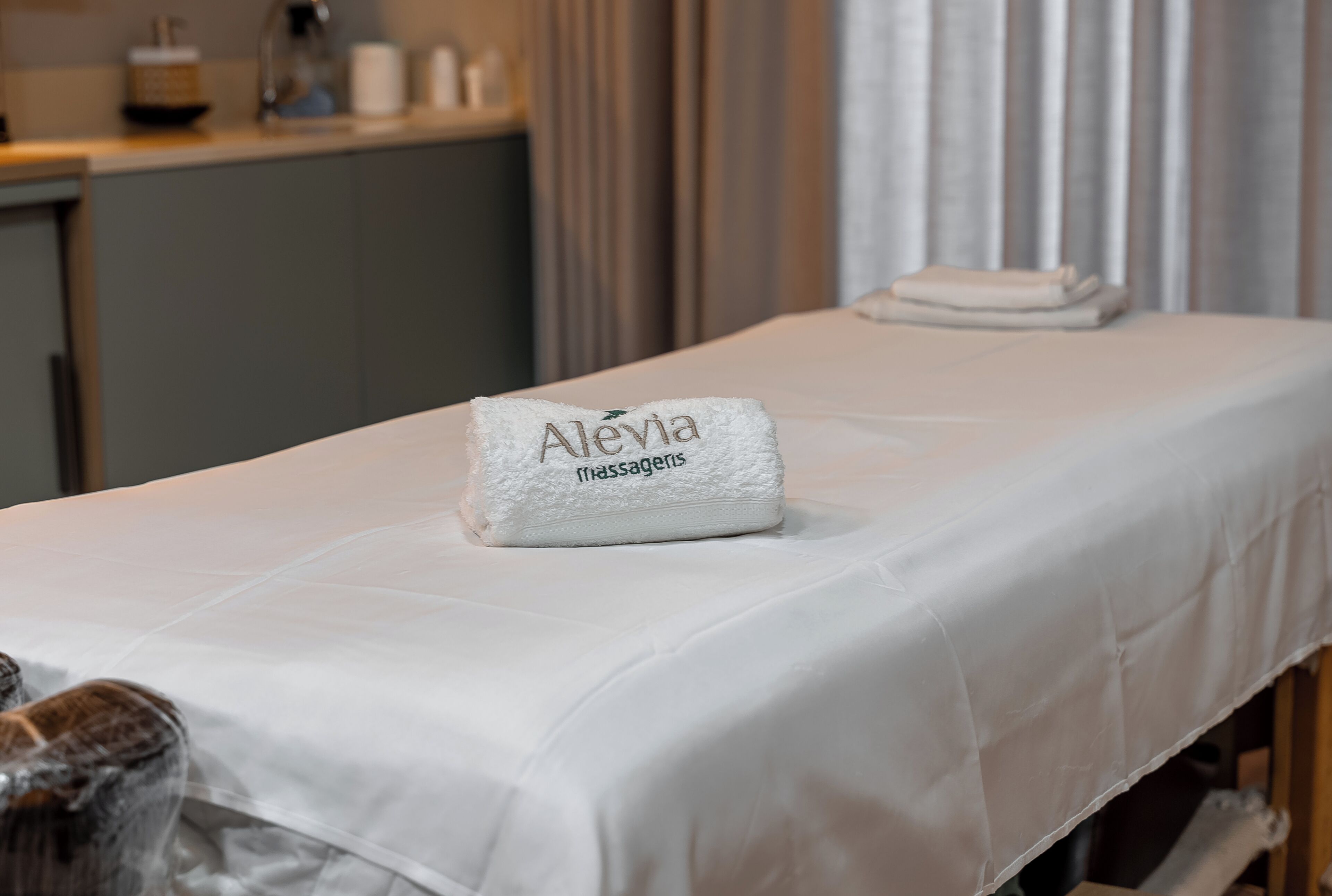 Una cama bien hecha con una toalla que dice "Alevia Massagien" y otra toalla doblada a un lado.