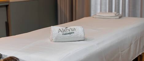 Una cama bien hecha con una toalla que dice "Alevia Massagien" y otra toalla doblada a un lado.