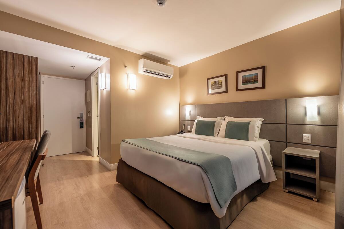 A hotel room with a bed, bedside tables, a desk, and a chair.