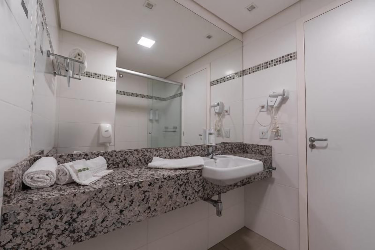 A bathroom with a granite countertop, a sink, a mirror, and a towel rack with towels.